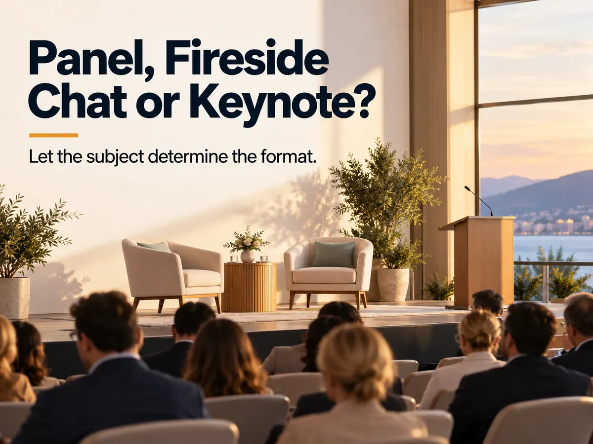 An audience faces a conference stage furnished with two armchairs, a side table and a lectern.