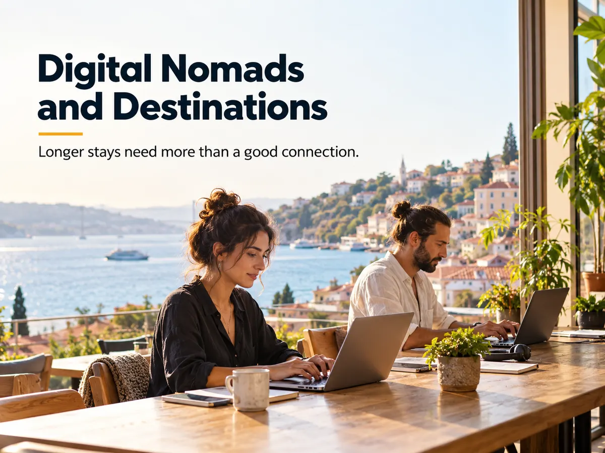 Two people work on laptops at a shared table beside windows overlooking a coastal settlement.