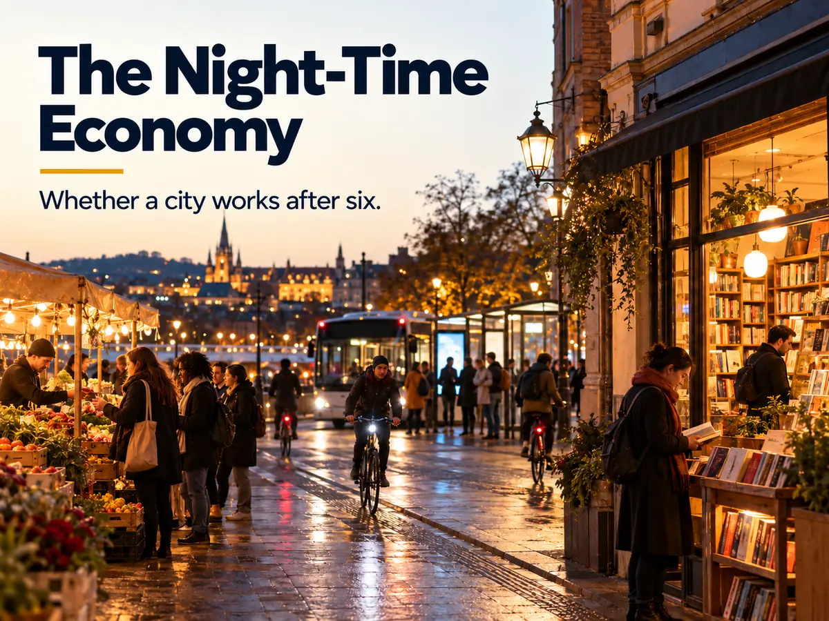A lively city street at night with an open bookshop, a food market, people on bicycles and a late bus at a lit stop